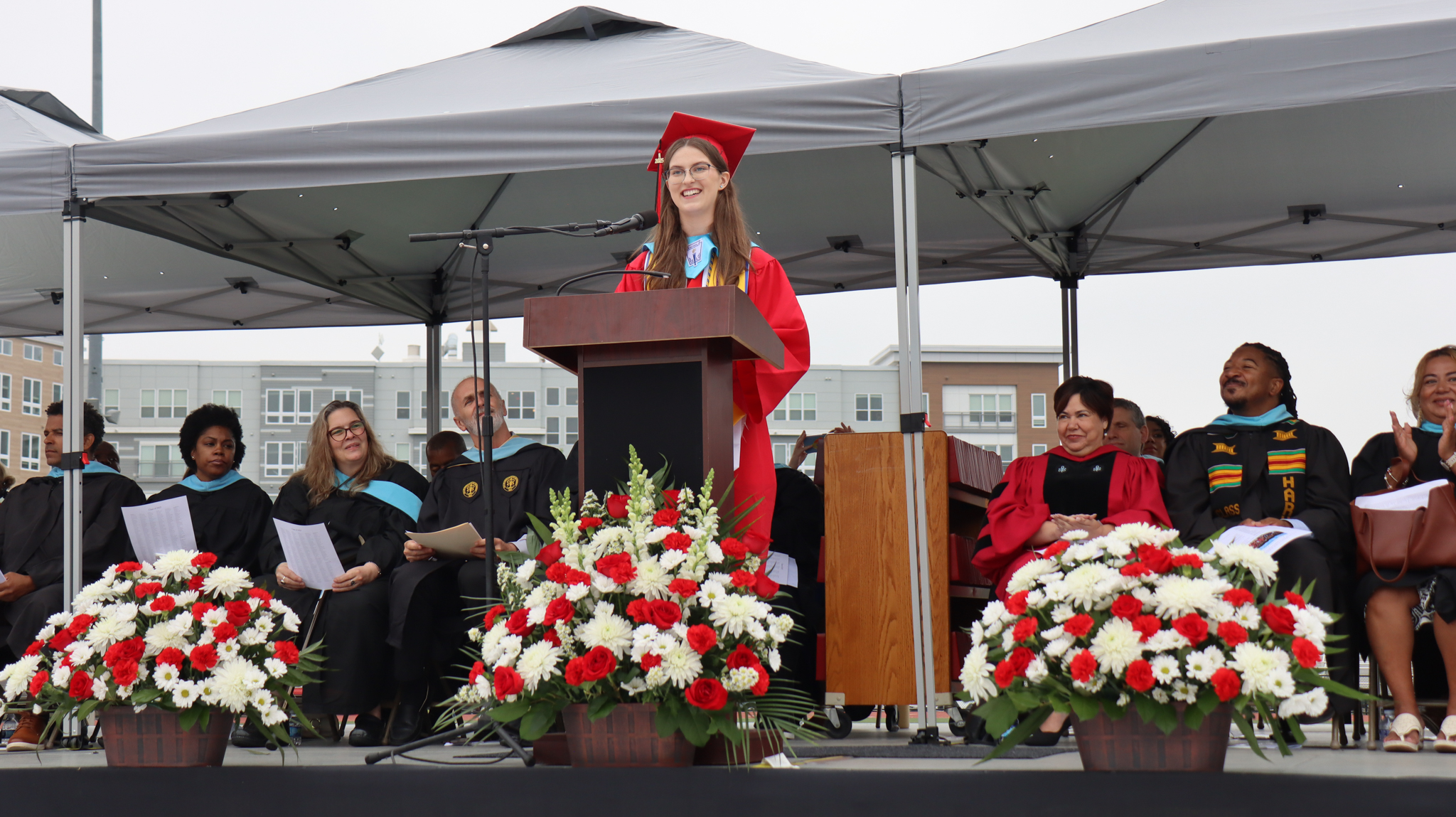 Valedictorian Holly Hatleberg standing at a podium giving a speech in a red Graduation cap and gown